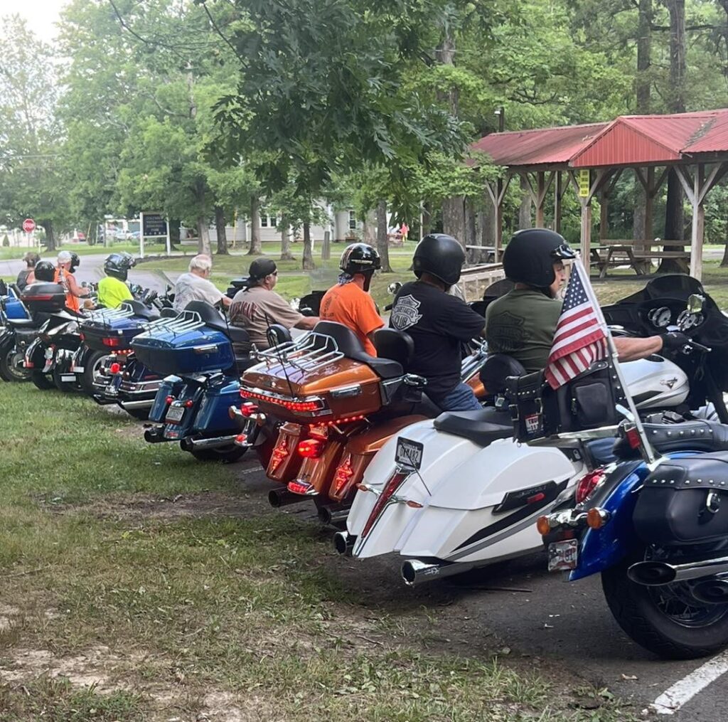 A group of people on motorcycles parked in the grass.